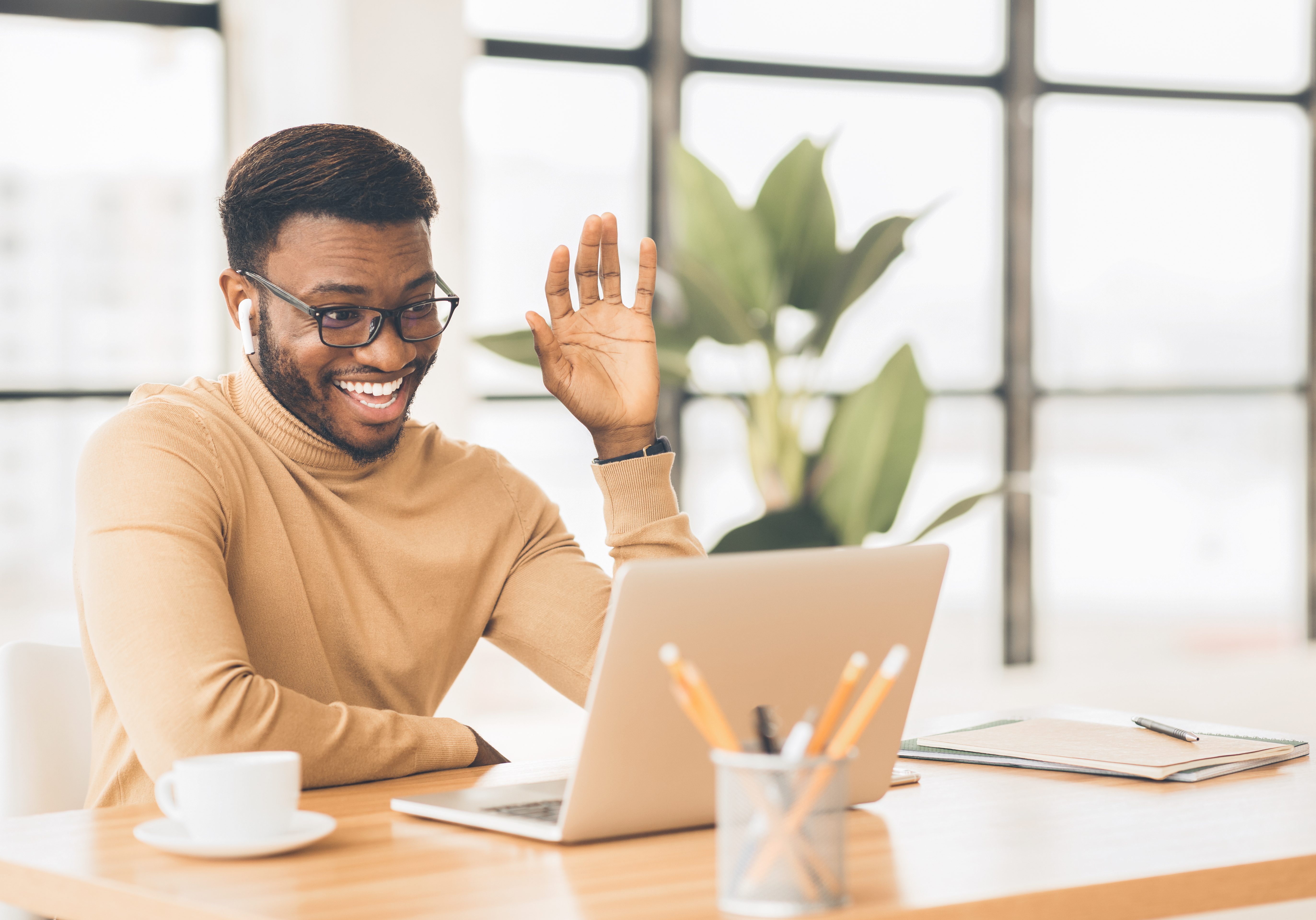 Happy African businessman making video call to family using laptop during coffee break in office, copy space